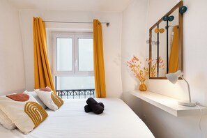 A hotel room with a bed, a window with yellow curtains, a bedside table with a lamp, and a mirror with decorative elements. - Sacré-Coeur view, 2 min from Paris, Netflix & Cosy (Clichy)