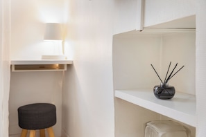 Minimalistinen huone, jossa on valkoinen hylly, lamppu, pieni jakkara ja aromadiffuusori.