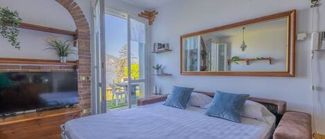 A bedroom with a large bed, a TV, a brick fireplace, and a view of the outdoors.