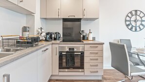 A modern kitchen with stainless steel appliances, a built-in oven, and a dining area with a table and chairs. - City Centre Luxury 1BDR Apt (Birmingham)