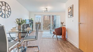 A modern living room with a glass dining table, chairs, a clock, and a large window. - City Centre Luxury 1BDR Apt (Birmingham)