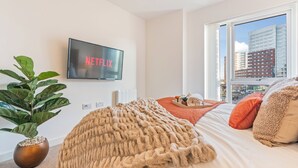 A bedroom with a bed, a large window, a plant, a blanket, and a TV displaying 'NETFLIX'. - City Centre Luxury 1BDR Apt (Birmingham)