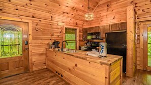 A wooden cabin interior with a kitchen area, including a refrigerator, coffee maker, and a window with blinds. - Cozy Cabin in Pigeon Forge, Hot tub & Scenic Views (Pigeon Forge)