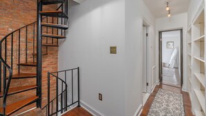 Un escalier avec un mur en briques, un couloir avec un tapis à motifs et une étagère blanche.