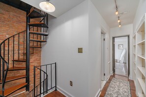 A staircase with a brick wall, a hallway with a patterned rug, and a white shelving unit. - Quiet Federal Hill 3BR - Walk to Hospitals, Stadiums, Dining and Nightlife (Baltimore)