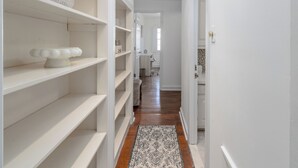 Un couloir avec des étagères blanches, un tapis à motifs et une porte donnant sur une salle de bain.