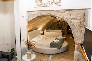 Un dormitorio con un arco de piedra, una cama redonda, un tocador y un espejo.