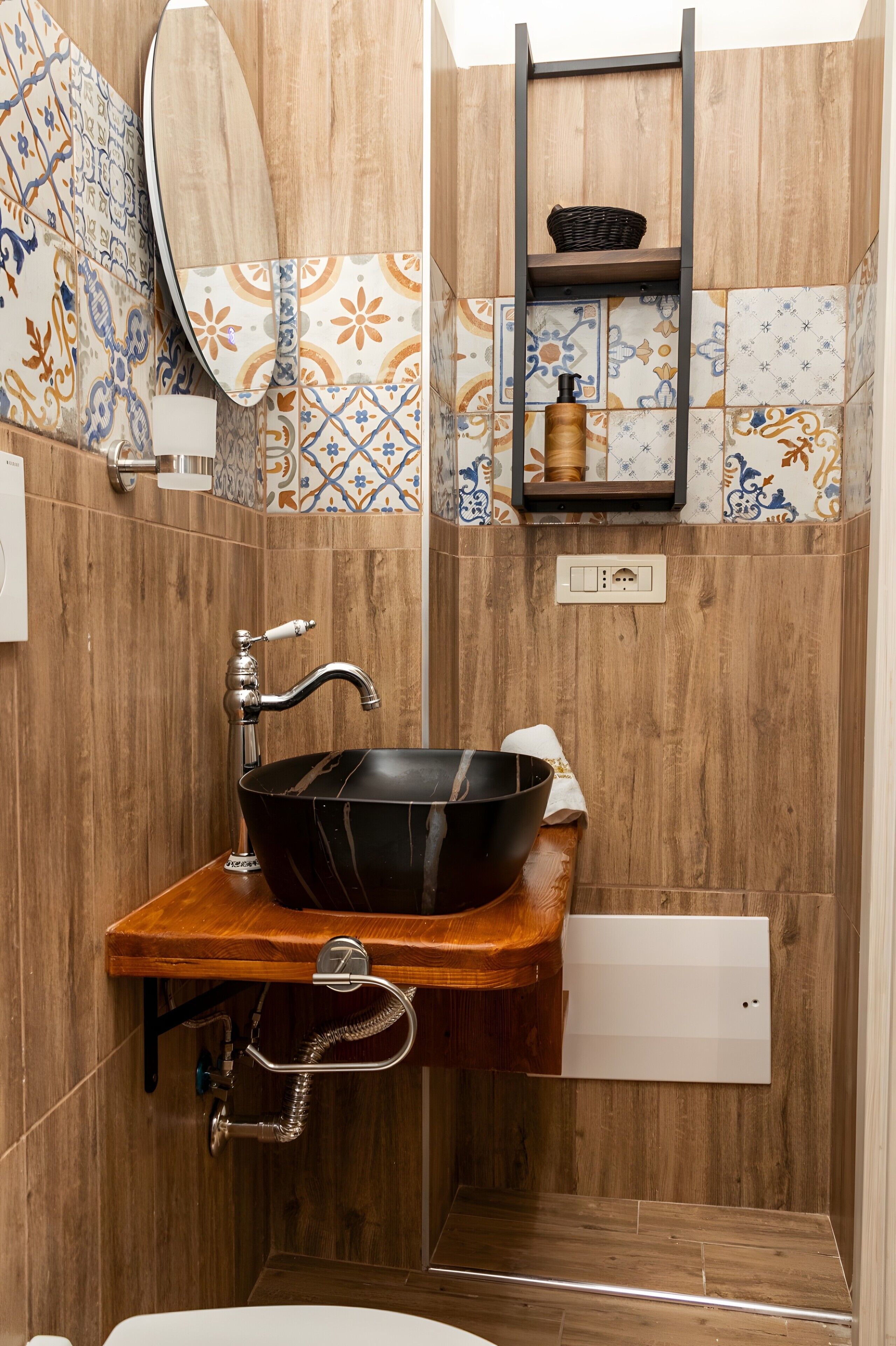 Een badkamer met een houten wastafelmeubel, een zwarte wasbak, een spiegel en een plank met een mand.