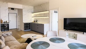 Een moderne woonkamer met een bank, een eettafel met plaatszetters, een televisie en een keuken met een marmeren achterwand.