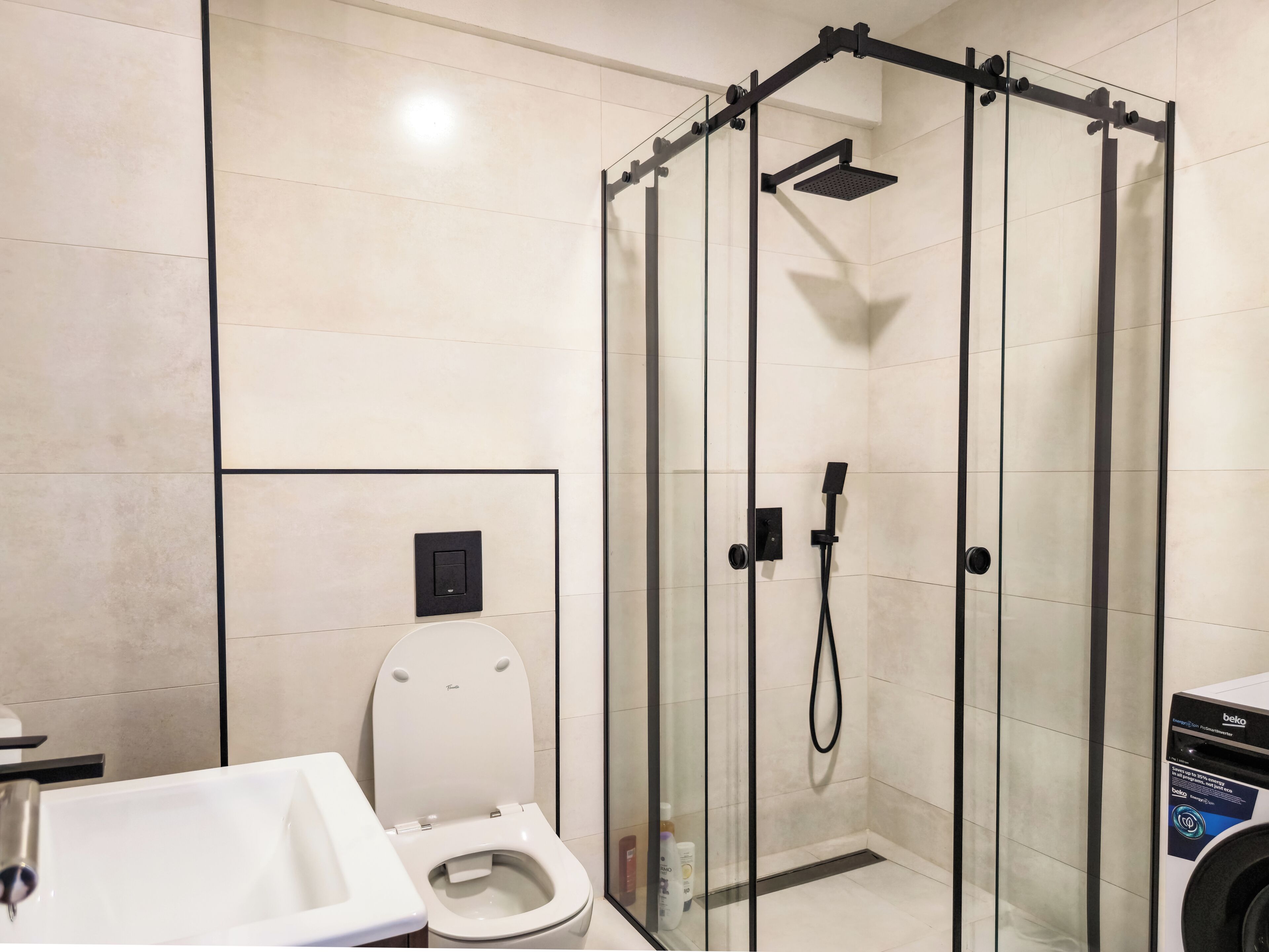A modern bathroom with a glass-enclosed shower, a toilet, and a sink.
