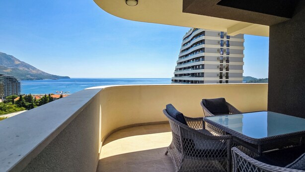 Een balkon met een glazen tafel en rieten stoelen, met uitzicht op een strand en de oceaan.