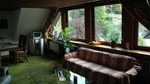 Une pièce comprenant un canapé, une table à manger, une chaise, un téléviseur et une fenêtre avec des plantes.