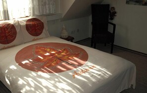 Ein Bett mit Blättermotiv und dem Schriftzug 'Autumn' auf der Bettdecke, ein Sessel und ein Fenster mit Vorhängen.