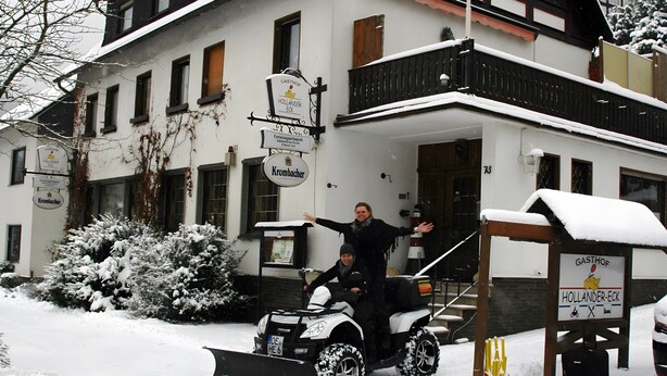 Un bâtiment dont l’entrée est recouverte de neige, avec une enseigne et un chasse-neige à proximité.