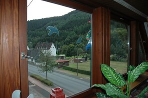 Ein Holzrahmenfenster mit Blick auf eine Straße, ein Gebäude und einen bewaldeten Hügel.
