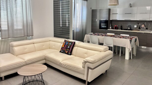 Una sala de estar moderna con un sofá modular, una mesa de comedor y una cocina con electrodomésticos de acero inoxidable.
