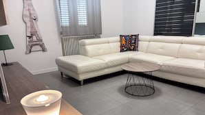 Una sala moderna con un sofá modular, una mesa redonda de centro, una lámpara y una obra de arte con la Torre Eiffel en la pared.