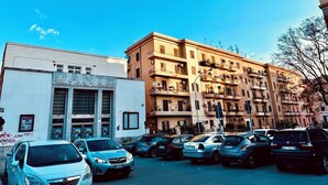 Un edificio de varios pisos con balcones, un cine y un estacionamiento con coches.