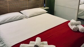 Habitación de hotel con una cama, una colcha roja, almohadas blancas, un cabecero de madera y una mesita de noche con una lámpara.