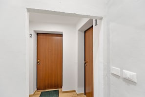Ein Korridor mit zwei Holztüren, einer weißen Wand und einem Lichtschalter.
