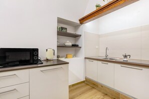 Une cuisine moderne avec des armoires blanches, un plan de travail en bois, un four à micro-ondes encastré, un évier et une étagère ornée d’objets décoratifs.