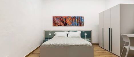 A modern bedroom with a bed, bedside tables, a desk, and a wardrobe.