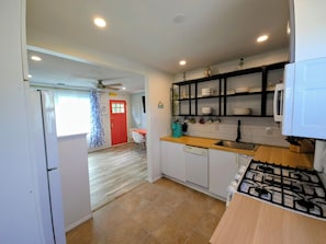 A compact kitchen with a gas stove, a sink, and a countertop. There is a red door leading to another room, and a ceiling fan is visible.
