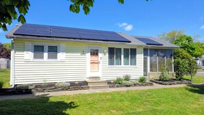 Una casa de una planta con paneles solares en el techo, una puerta principal y un pequeño jardín.