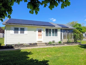A single-story house with solar panels on the roof, a front door, and a small garden area.