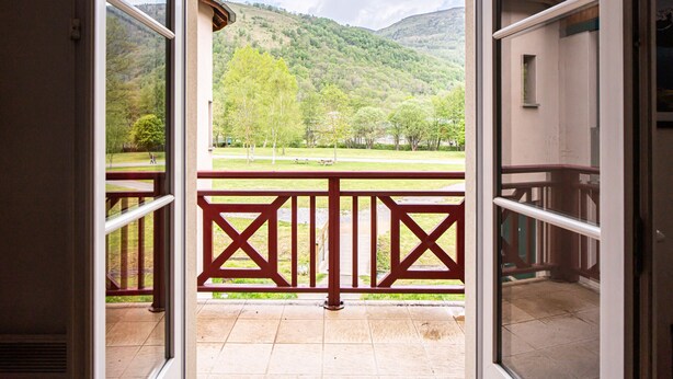Uitzicht vanaf een balkon met een balustrade, betegelde vloer en een landschap van bomen en heuvels.