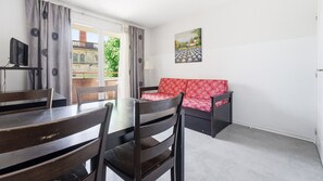 A room with a dining table, chairs, a sofa, a painting, and a view of greenery outside. - Apartment for 4 people, with a balcony (Grasse)