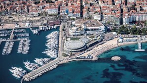 Vista aerea di una città costiera con un porto turistico, edifici e una struttura circolare.