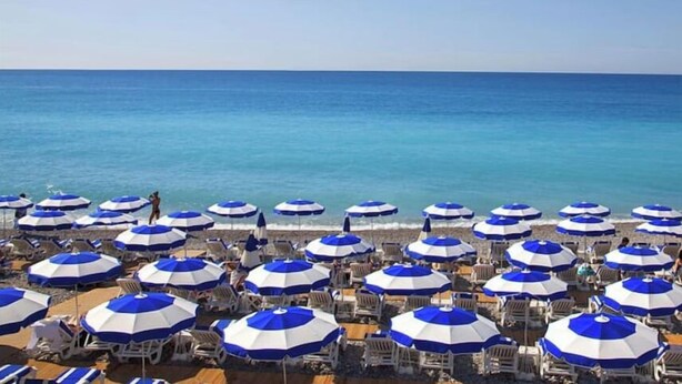 Una spiaggia con file di ombrelloni e lettini blu e bianchi.
