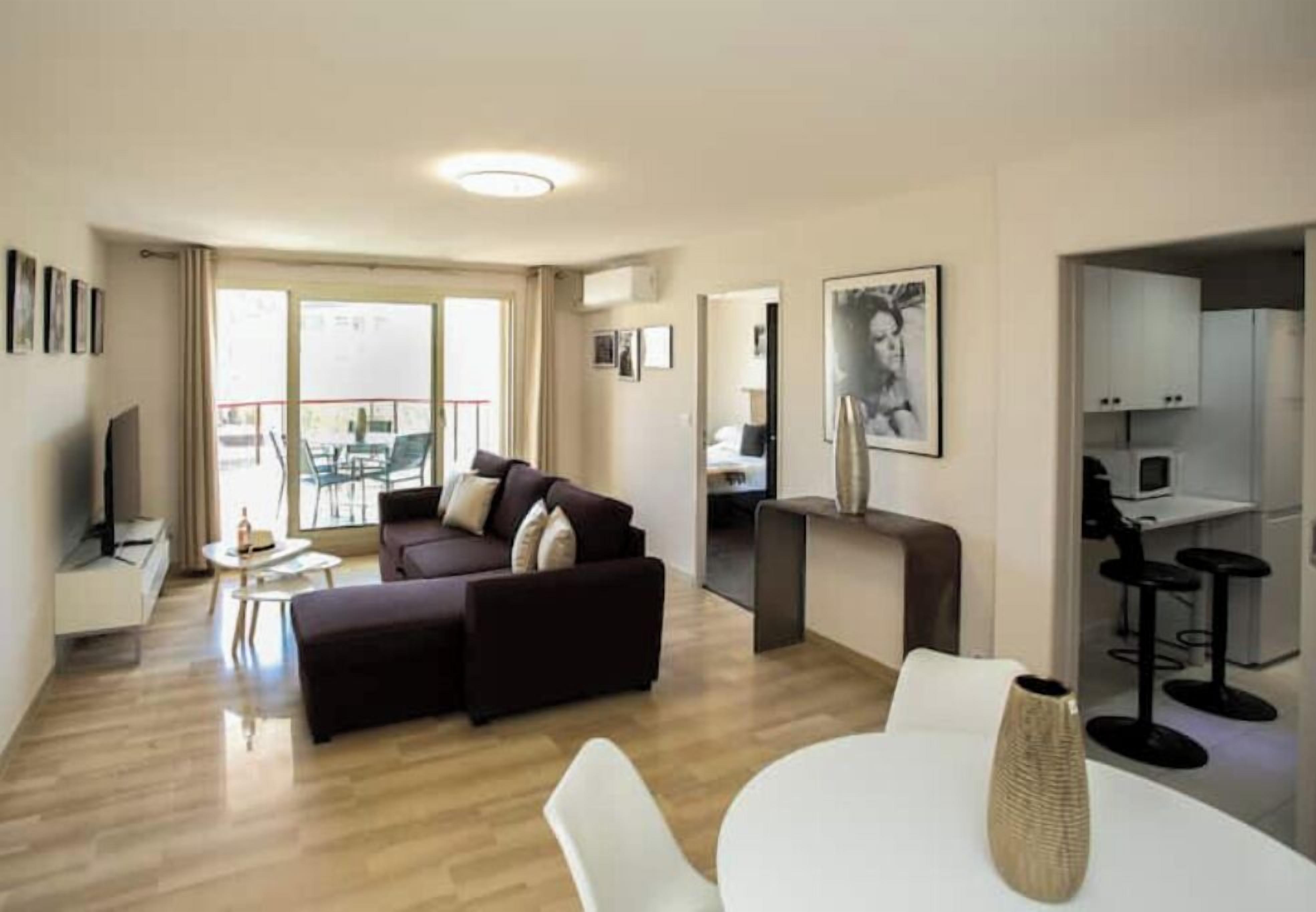 A modern living room with a sofa, a dining table, and a kitchen area visible through an open door.