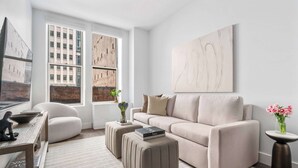 A modern living room with a sofa, ottomans, a coffee table, and a large abstract painting on the wall. - 17John: Superior 2 Bed W/D in unit + GYM + Lounge (New York)