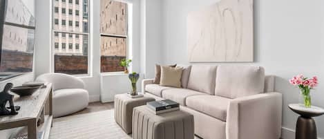 A modern living room with a sofa, ottomans, a coffee table, and a large abstract painting on the wall.
