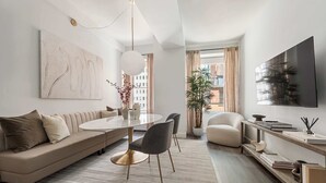 A modern living room with a sofa, dining table, chairs, a TV, and a plant. - 17John: Signature 3 Bed W/D in unit + GYM + Lounge (New York)