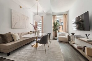 A modern living room with a sofa, dining table, chairs, a TV, and a plant.