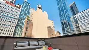 Una terraza en la azotea con un sofá, una mesa redonda con bebidas y vistas a rascacielos de la ciudad.