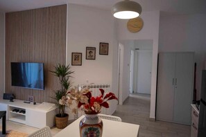 A modern living room with a flat-screen TV, a potted plant, a vase with flowers, and a dining area.