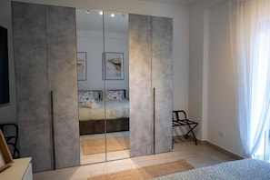 Ein Schlafzimmer mit großem Kleiderschrank, einem Bett, einem Sessel und einem Fenster mit Vorhängen.