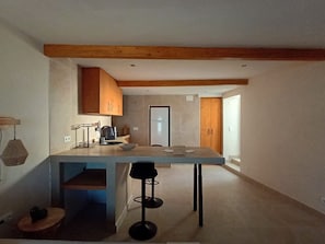 A modern kitchen with wooden beams, a large island, and a bar stool. - Modern Studio Almada | Near Lisbon & Sea (Trafaria)
