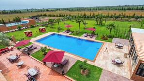 A rectangular swimming pool with adjacent lounge areas, outdoor tables, and umbrellas.