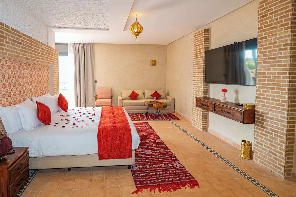 Ein Hotelzimmer mit Backsteinwand, einem Bett mit roten Kissen, einer Couch, einem Fernseher und einer Wanddekoration.