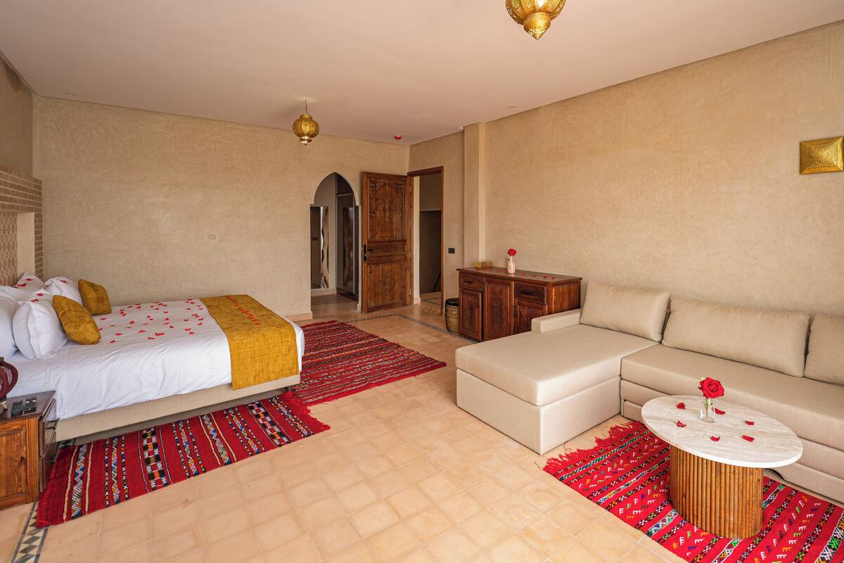 A hotel room with a bed, sofa, round coffee table, and a decorative rug.