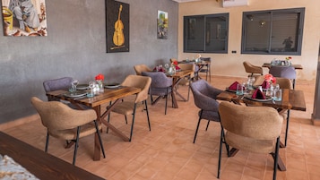Un restaurante con varias mesas y sillas, piso de baldosas y obras de arte en las paredes.