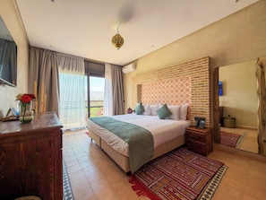Ein Schlafzimmer mit einem großen Bett, einer Holzkommode, einem Nachttisch, einem verzierten Kopfteil und Blick durch ein großes Fenster.