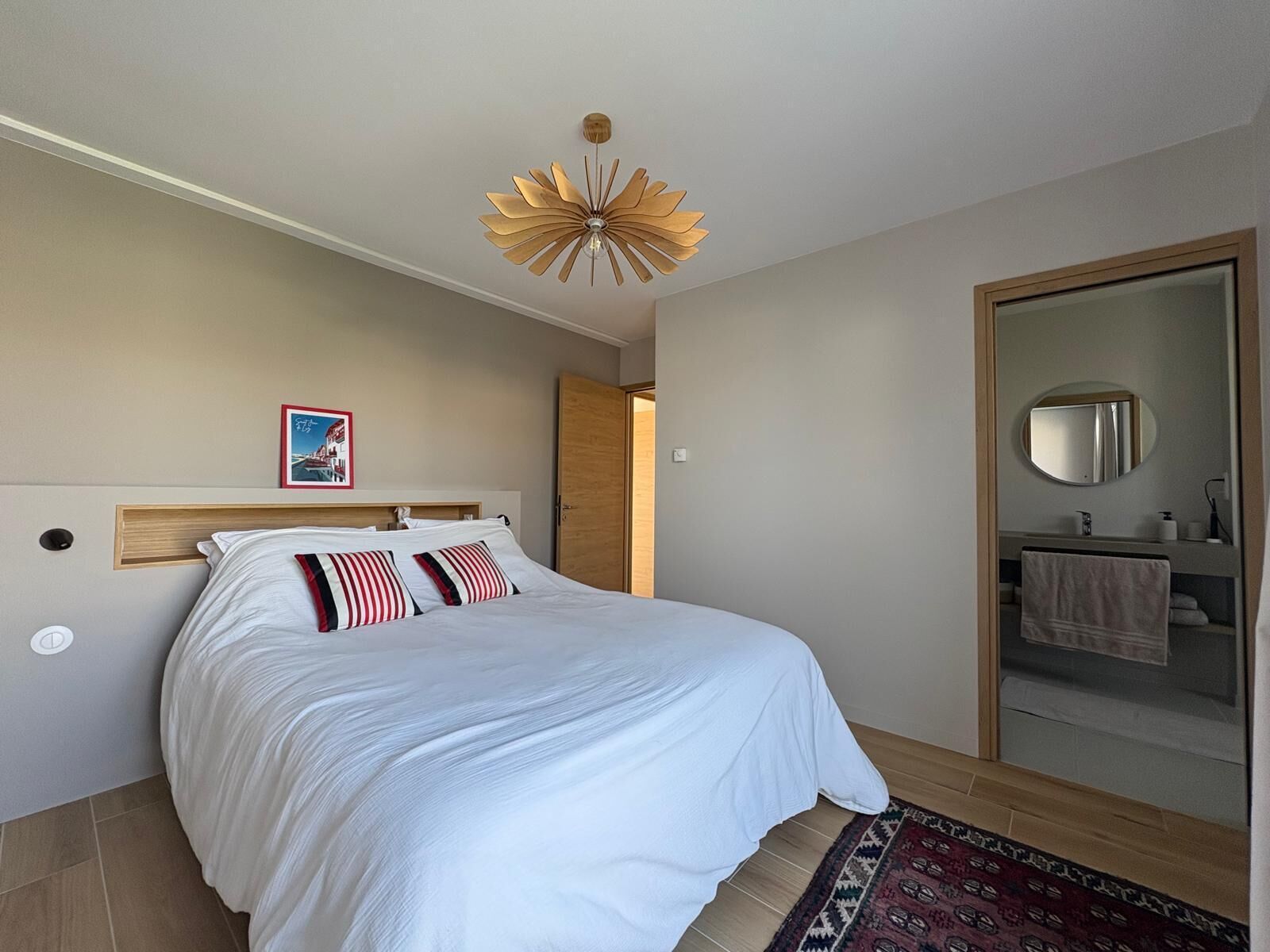 Ein Schlafzimmer mit Bett, Holz-Kopfteil, Deckenventilator, Spiegel und einer Tür zum Badezimmer.