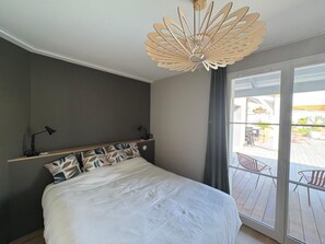 Ein Schlafzimmer mit einem Bett, einem Nachttisch, einer Schreibtischlampe, einem Deckenventilator und einer Glastür, die zu einem Außenbereich führt.