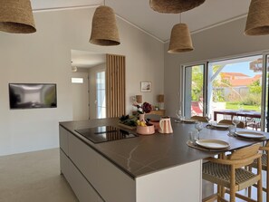 A modern kitchen with a central island, hanging woven light fixtures, a flat-screen TV, and a view of the outdoors. - Modern villa with a pool (Châtelaillon-Plage)